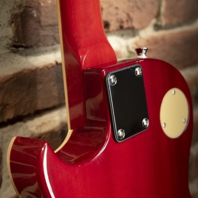 Guitarra elétrica vermelha com placa preta na parte traseira encostada numa parede de tijolos