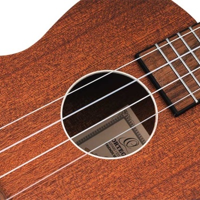 Ukulele de madeira castanho avermelhado com 4 cordas brancas e rótulo visível no interior