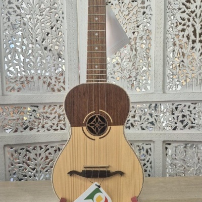 Cavaquinho em madeira com suporte vermelho sobre superfície de madeira e fundo decorativo branco