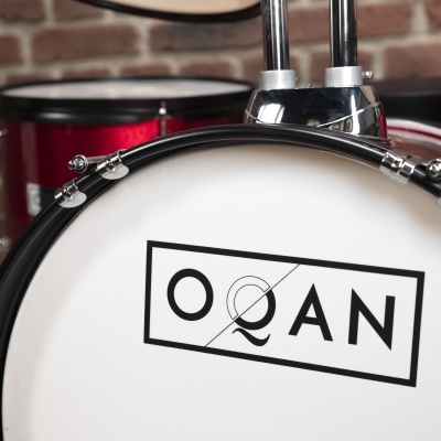 Bateria musical vermelha com pele branca e marca OQAN no bumbo