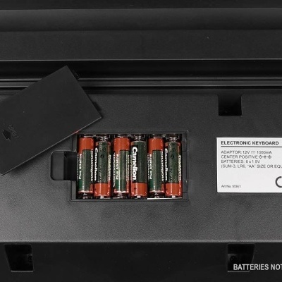 Compartimento de pilhas aberto de teclado eletrônico com quatro pilhas e etiqueta de especificações