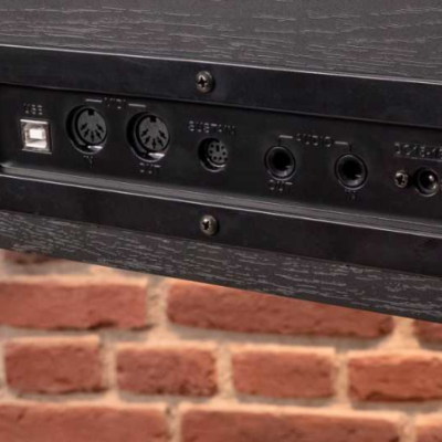 Painel com conectores USB, MIDI e jack em madeira escura, fundo de tijolos vermelhos