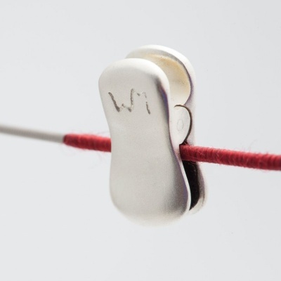 Presilha metálica prateada com letras WI segurando fio vermelho