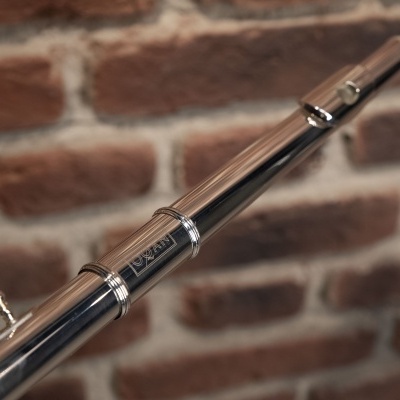 Flauta prateada com acabamento brilhante diante de parede de tijolos