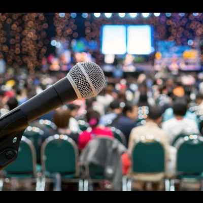 Microfone negro em foco com público desfocado em conferência