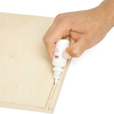 Mão a aplicar cola branca na lateral de uma prancha de madeira clara