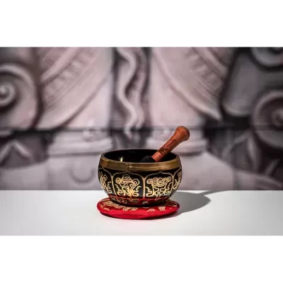 Tigela preta e dourada com batedor de madeira sobre suporte vermelho bordado.