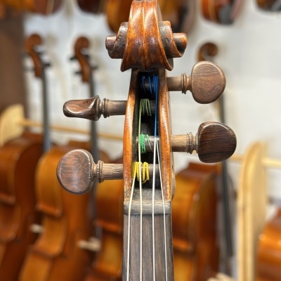 Cabeçote de violino castanho com cordas coloridas e múltiplos violinos ao fundo