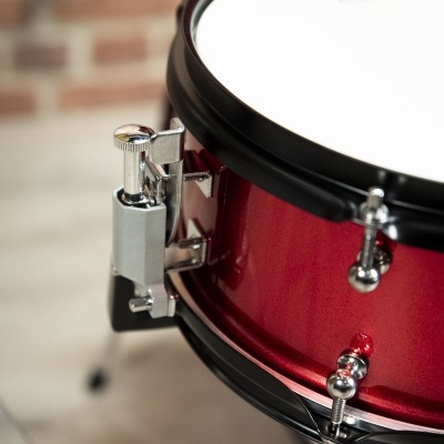 Caixa de bateria vermelha com aro e parafusos cromados, pele branca, parede de tijolos ao fundo