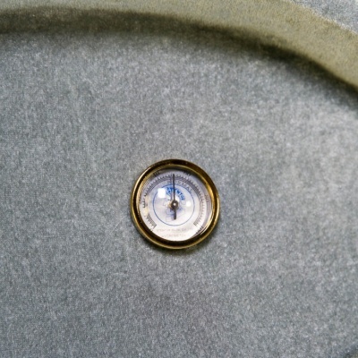 Barómetro circular com moldura dourada numa superfície cinzenta