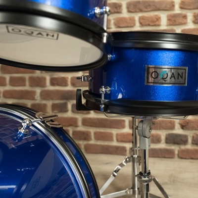 Tambores azuis metalizados com detalhes cromados sobre suporte metálico em frente a parede de tijolos.