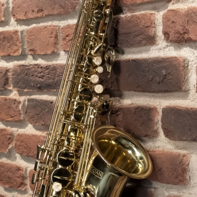 Saxofone tenor dourado encostado numa parede de tijolos vermelhos