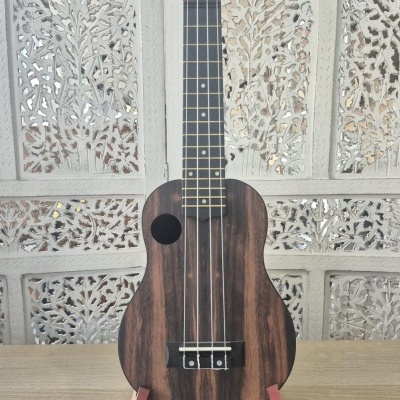 Ukelele de madeira escura com cordas e pestana preta em suporte vermelho sobre mesa clara