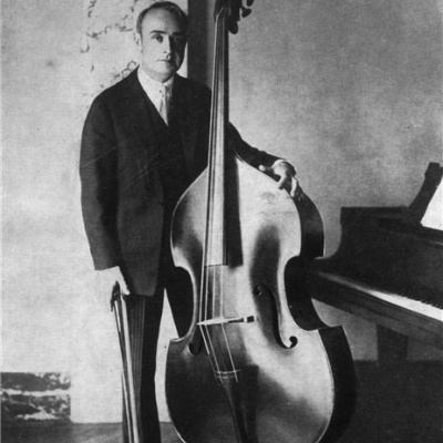 Homem segurando contrabaixo acústico junto a piano de cauda em ambiente interno