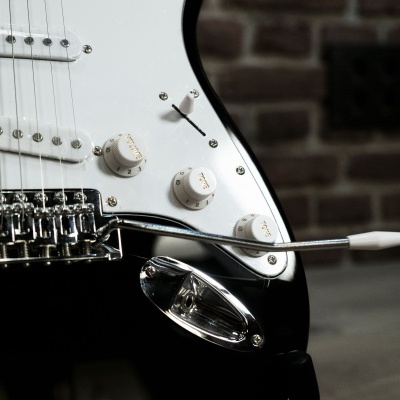 Guitarra elétrica preta com detalhes brancos e cromados encostada num ambiente interno