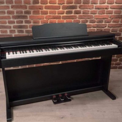 Piano digital preto com 88 teclas e três pedais, com fundo de parede de tijolos