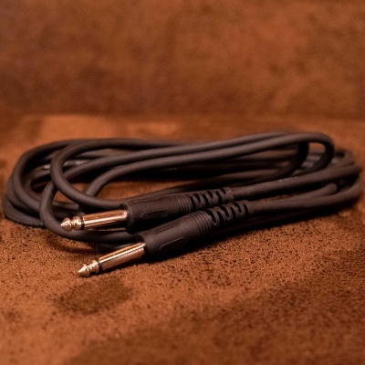 Cabo preto com conectores jack de 6,35 mm sobre superfície castanha.