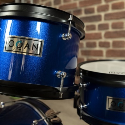 Conjunto de tambores azuis metálicos com etiquetas 'OGAN' em fundo de parede de tijolos.