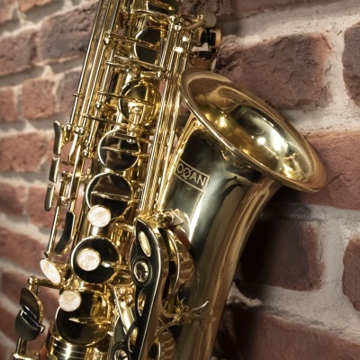 Saxofone dourado com teclas pretas encostado a parede de tijolos vermelhos