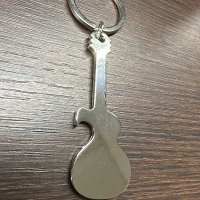 Chaveiro metálico em forma de guitarra sobre madeira escura