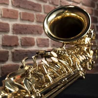 Saxofone tenor dourado numa superfície preta com parede de tijolos vermelhos ao fundo