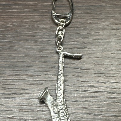 Porta-chaves metálico prateado em forma de saxofone sobre madeira escura