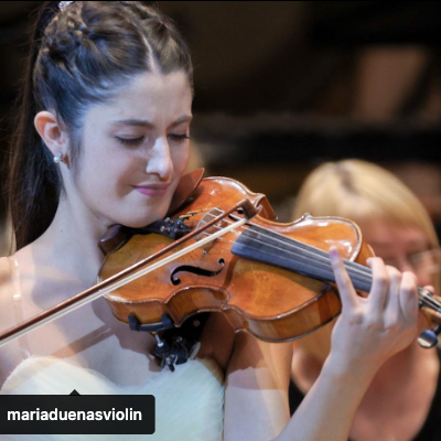Jovem mulher tocando violino de madeira castanha com partes pretas num concerto