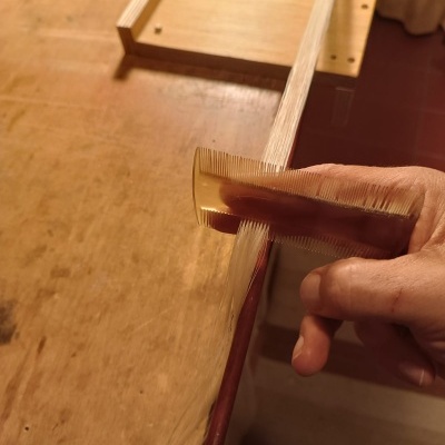 Mão a pentear fios loiros com pente transparente sobre mesa de madeira