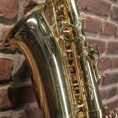 Saxofone dourado com gravuras decorativas encostado em parede de tijolos