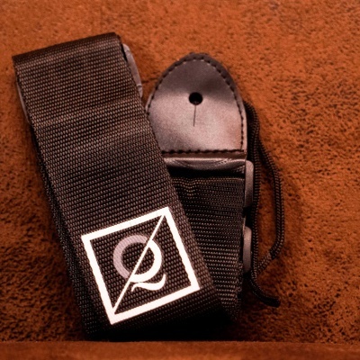 Correia para guitarra ou baixo preta com logotipo branco sobre chão castanho