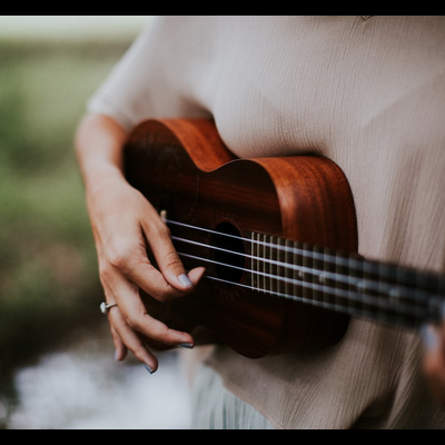 Pessoa a tocar um ukulele de madeira castanha com fundo verde desfocado