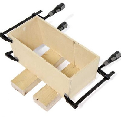 Moldura de madeira clara sendo montada com grampos pretos