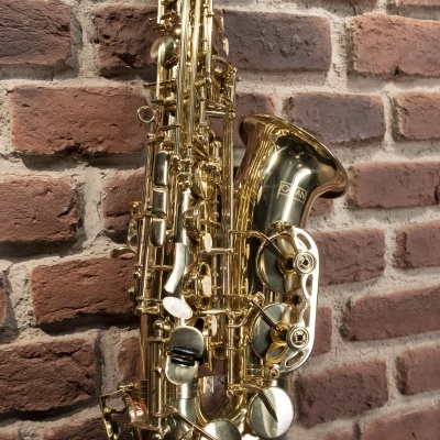 Saxofone dourado encostado numa parede de tijolos vermelhos.