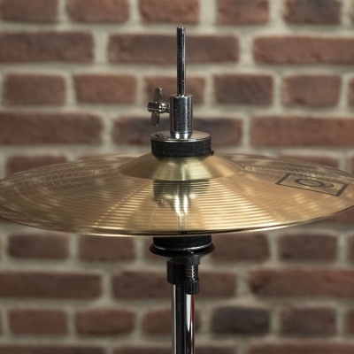 Prato de percussão dourado montado em suporte com parede de tijolos ao fundo