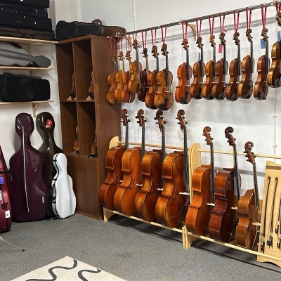 Instrumentos musicais em loja com violinos, violas e violoncelos em madeira e capas para instrumentos