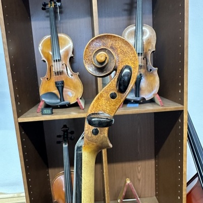 Violino envelhecido em primeiro plano com estante contendo outros violinos ao fundo