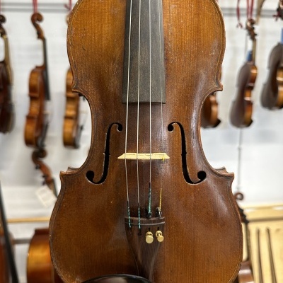 Violino castanho de madeira com quatro cordas segurado à frente de várias guitarras penduradas