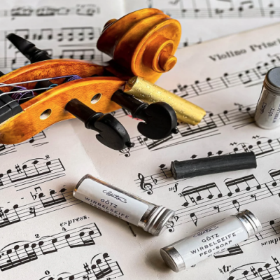 Violino em madeira clara com cravelhas pretas sobre partitura musical com caixas metálicas cilíndricas