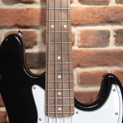 Guitarra elétrica preta com braço de madeira clara e fundo de tijolos