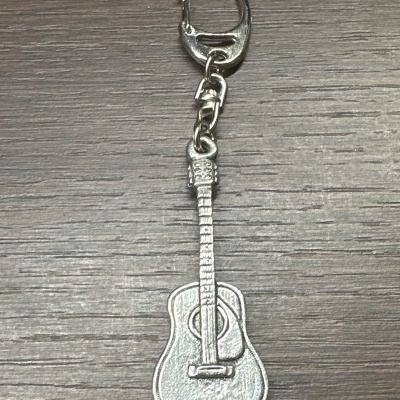 Porta-chaves prateado em forma de guitarra acústica sobre mesa de madeira.