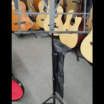 Suporte de partitura musical preto em tripé com bag preta e guitarras acústicas ao fundo
