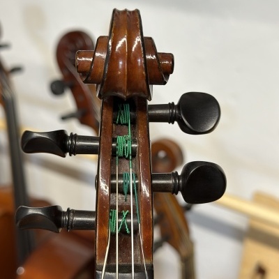 Cabeça de violino em madeira com cravelhas negras e cordas verdes, fundo desfocado com outros violinos