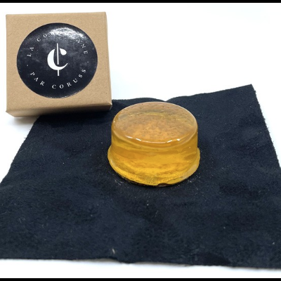 Produto redondo amarelo translúcido sobre pano preto com caixa de cartão castanho ao lado