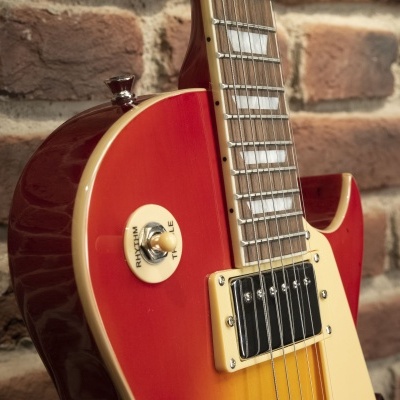 Guitarra elétrica vermelha e amarela com detalhes creme perto de parede de tijolos