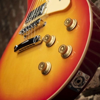 Guitarra elétrica vermelha e amarela encostada numa parede de tijolos