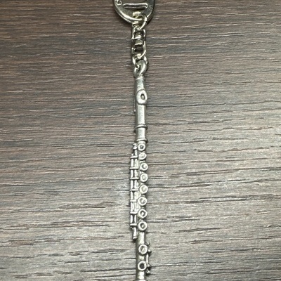 Chaveiro metálico prateado em forma de flauta sobre madeira escura