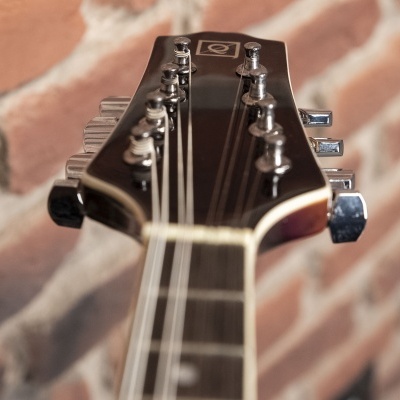 Cabeça de guitarra preta com tarraxas cromadas junto a parede de tijolos