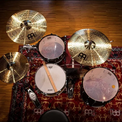 Conjunto de bateria com pratos Meinl, peles Remo, baquetas e tapete decorativo sobre chão de madeira