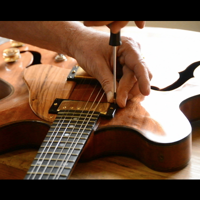 Pessoa a afinar guitarra elétrica de corpo oco em madeira com chave de fendas