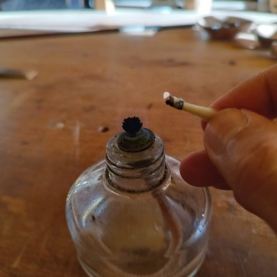 Frasco de vidro com pavio queimado e mão segurando fósforo aceso